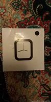 Front of sealed white smartwatch box with printed watch-face icon