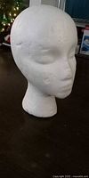 White styrofoam mannequin head angled on dark tabletop