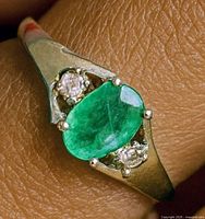 Ring on finger showing emerald and accent stones