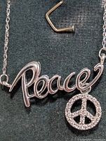 Close-up of pendant showing Peace script and diamond peace-sign charm