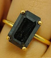 Top view of ring on finger showing rectangular black diamond and gold prongs