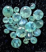 Group of round and pear cut alexandrite gemstones on black background showing bluish-green hue