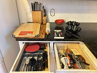 Countertop view showing knife block, cutting boards, rolling pin, mixing bowl, taco salad molds and open drawers with utensils