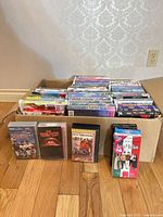 Cardboard box and loose tapes showing quantity and mix of titles including Disney clamshells and slipcases