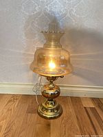 Lamp illuminated showing brass base, amber glass shade, clear chimney