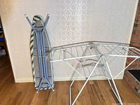 Ironing board standing upright next to unfolded drying rack