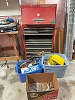 Red standing tool chest with two totes of tools and a cardboard box in front