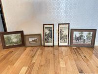 five of the six framed artworks standing on floor; shows variety of frames and subjects