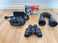Three binoculars displayed with Bushnell box and Minolta case