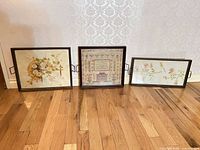 Front view of all three framed needlework pieces on floor showing design and size relationship
