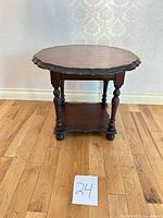 Front view of round end table showing scalloped top, turned legs, lower shelf
