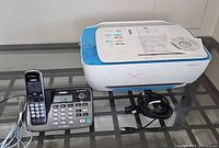 HP DeskJet 3630 printer, Uniden phone base and handset, cables on glass surface
