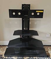 Front view of black metal TV stand with wall-mount bracket and three shelves
