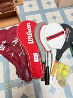 Multiple rackets with covers and bag of tennis balls on floor