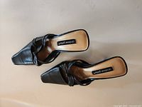 Top view of both black leather slide heels showing square toe, bow detail, insole branding