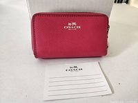 Front view of pink Coach double-zip card wallet with logo and info card