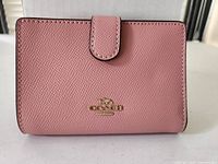 Front view showing pink pebble leather surface, snap tab, gold Coach logo