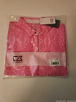 Front view of packaged pink/white Cutter & Buck women’s golf shirt with tags visible