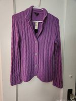 Front view of lilac cable-knit sweater jacket on hanger showing three-button closure and tag