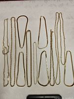 Twelve gold-tone chain necklaces laid out vertically