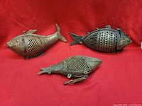 Three brass fish-form containers on red background