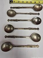 Five matching silver-plated souvenir spoons lined beside tape measure