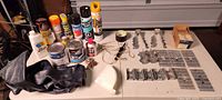 overall lot on table showing spray cans, paint cans, drill bits, joist hangers, collated nails, funnel, chain and rubber sheet