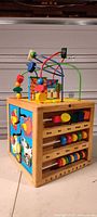 Full view of wooden activity cube showing bead maze on top and side panels with gears and counting sliders