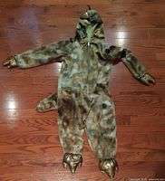 Front view of dinosaur costume laid flat showing hood, zipper, tail, claws, and foot covers