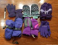 All six pairs of gloves and mittens arranged on floor with marker for scale