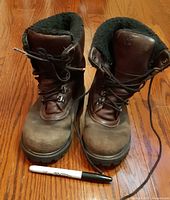 Front view of both boots showing lacing, toe scuffs, fleece lining, marker for scale