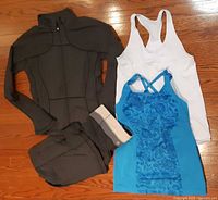 All four Lululemon items laid out: dark grey jacket, pants, white tank, blue tank
