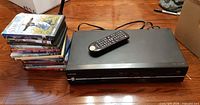 Front view of Toshiba combo unit, remote on top, stack of DVDs