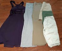 All six garments laid flat: purple dress, grey pants, khaki pants, skirt, shorts