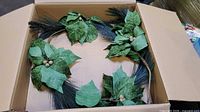 Wreath in box showing green fabric leaves, gold berries, plastic pine sprigs