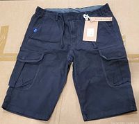Front view of black cargo shorts showing front pockets, drawstring and attached tag