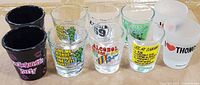 Front and angled top view of all ten shot glasses showing materials, prints, and condition