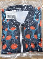 Sealed package showing folded polo shirt with white zipper and red/orange dot pattern on dark teal/navy field