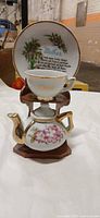 Front view of miniature teapot, cup, saucer on wooden stand displaying floral design and gilt trim