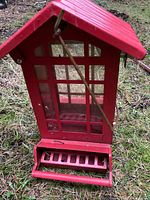 Front view of red metal bird feeder showing windowed seed reservoir, perch tray and hanging rod