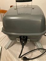 Front view of grey electric grill showing power cord and legs