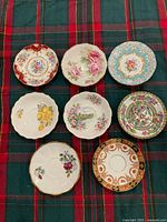 Eight assorted bone-china saucers displayed on tartan cloth