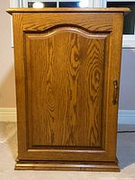 Front view of solid oak cabinet showing single door and brass-tone latch.