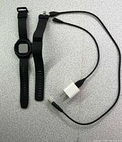 Garmin Approach S12 watch, Fitbit Charge band, USB charging cable, wall adapter on tabletop