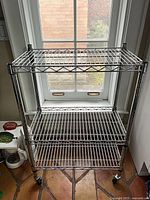 Front view of the three-shelf stainless wire rack showing shelves, posts, and casters