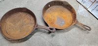 Two rusted cast iron skillets side by side