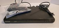 Front view of Samsung Blu-ray player with remote and power cord