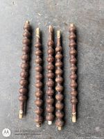 Five dark stained wooden spindles with beaded pattern laid out side by side showing full length and tenon ends