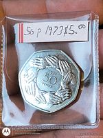 Reverse of 1973 50p coin with nine hands design in plastic holder