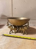 Side view showing brass bowl on three elephant base with measuring tape